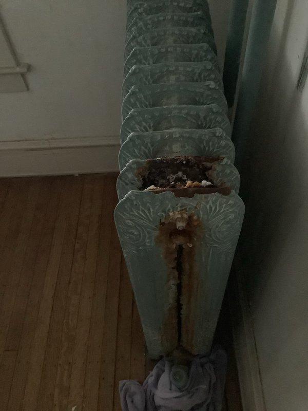 Responded to service call for 8-year-old boiler system with significant corrosion issues. Upon inspection, found severe deterioration on cast iron radiator including a penetration hole with substantial rust damage. Basement inspection revealed poor maintenance conditions with multiple pipe systems requiring attention.