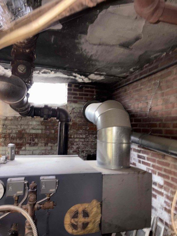 Performed inspection and assessment of aging 20-year-old commercial steam boiler system requiring replacement. Evaluated electrical service panel and existing boiler installation against brick wall in utility area. Documented current configuration with photographs to develop comprehensive replacement proposal.