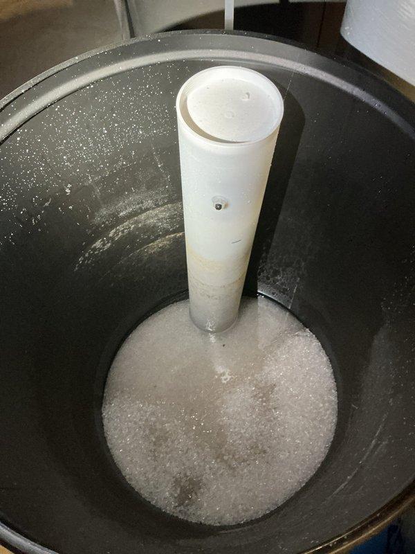 Completed salt delivery and replenishment for water softening system. Filled brine tank with fresh water softener salt pellets after observing low salt levels and foam accumulation at the bottom of the tank. System is now properly charged for continued water treatment operation.