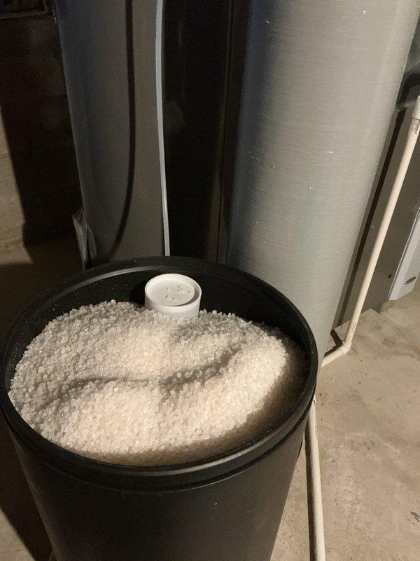 Completed salt delivery and replenishment for water softening system. Filled brine tank with fresh water softener salt pellets after observing low salt levels and foam accumulation at the bottom of the tank. System is now properly charged for continued water treatment operation.