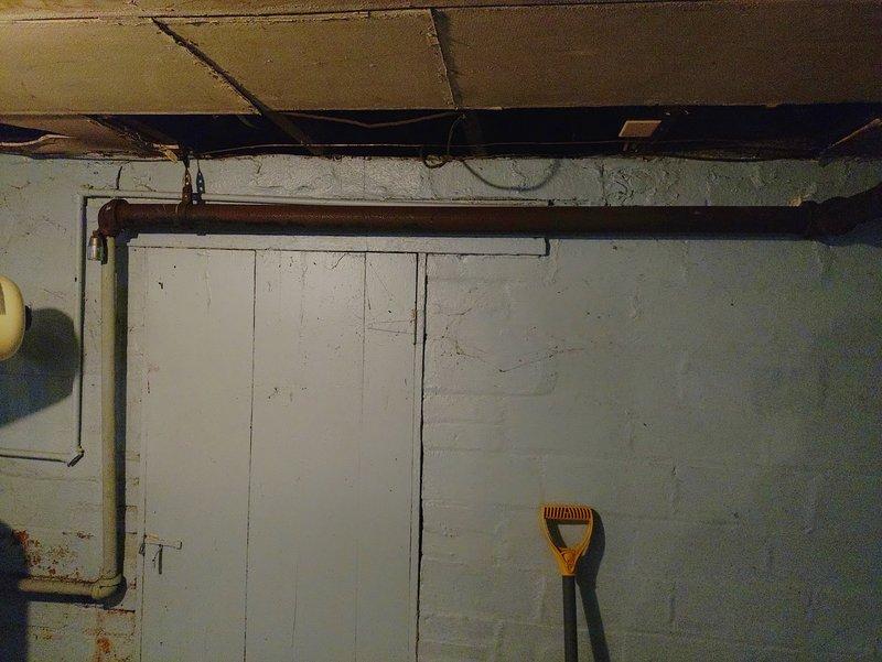 Conducted inspection of tanked water heater system due to high readings indicating potential leak. Examined copper supply lines and connections in utility area. Documented condition of aging radiator pipe with valve fitting and surrounding plumbing infrastructure for further assessment.