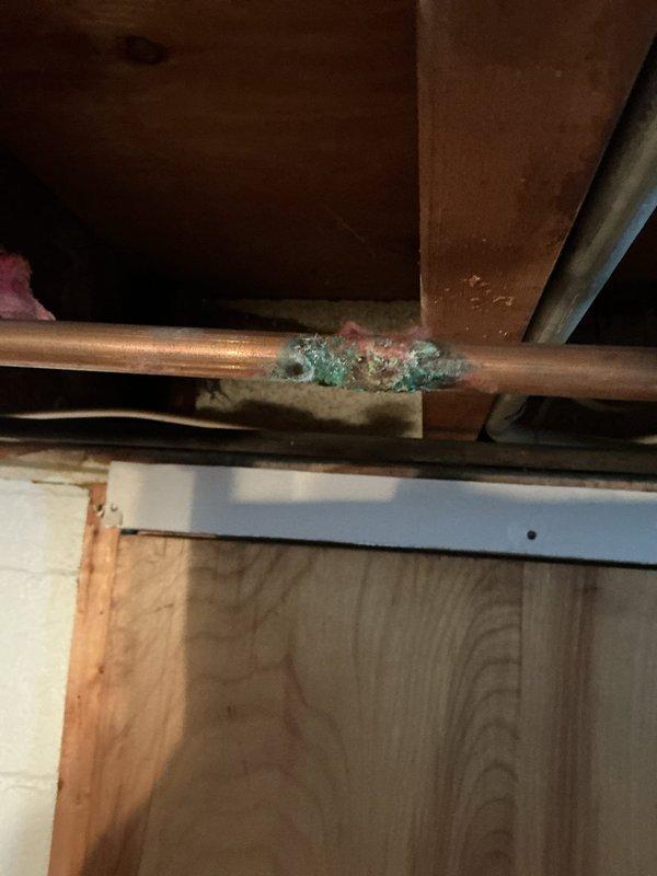 Located and repaired a pinhole leak in corroded copper supply line in basement. Removed deteriorated red insulation to access the affected pipe, which showed significant greenish-blue oxidation. Replaced damaged section of pipe to prevent further water damage to surrounding wooden structural elements.