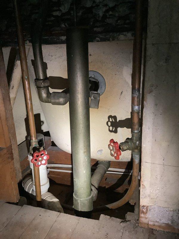 Responded to service call regarding leaking plumbing stems for hot and cold water fixtures in bathroom sink. Inspected the bathroom installation featuring six porcelain cross-handle fixtures (three upper and three lower) with signs of normal wear. Further examination of the utility area revealed copper pipes with soldered joints and a central cast iron pipe with two red valve handles controlling water flow through the system.