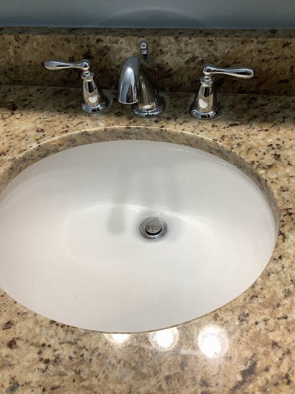 Successfully installed new three-piece chrome faucet assembly in bathroom with undermount white oval basin. Inspected and serviced noisy drain, ensuring proper function of the chrome push-button drain stopper. Verified all connections at the PVC P-trap and supply lines for leaks, confirming complete resolution of drainage noise issue.