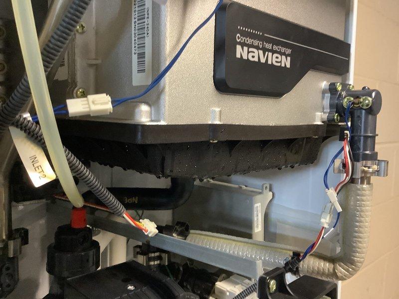 Performed routine tankless water heater descaling service on Navien condensing heat exchanger unit. Identified and documented significant condensation along bottom edge of unit and rust-colored staining/water damage at PVC pipe connection point. Completed flush procedure to remove mineral buildup and improve system efficiency.