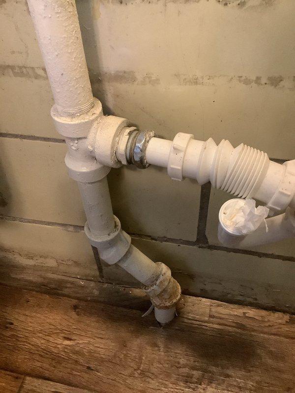 Completed installation of new sanitary tee on existing galvanized pipe using two no-hub bands, rotating the tee 180 degrees to accommodate future sink installation. Verified proper connection points and alignment of PVC sections with the existing drain system in basement utility area.