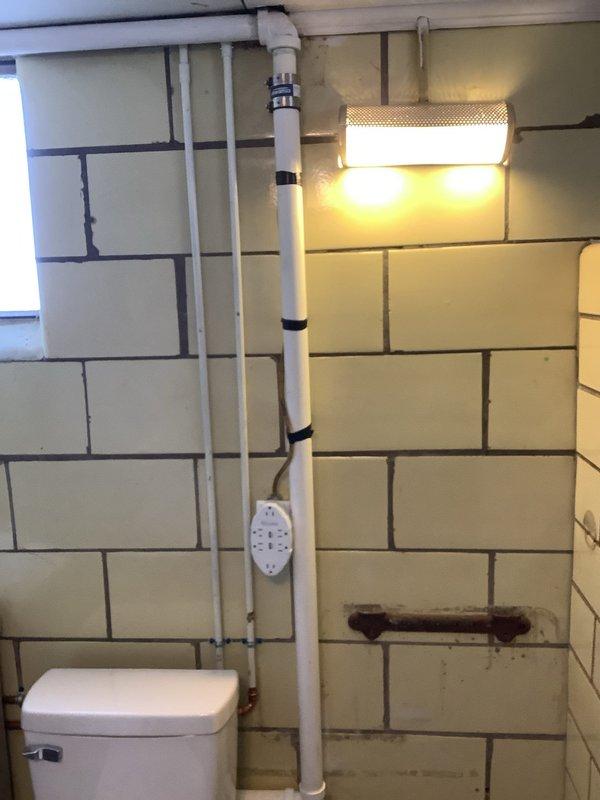 Completed installation of new sanitary tee on existing galvanized pipe using two no-hub bands, rotating the tee 180 degrees to accommodate future sink installation. Verified proper connection points and alignment of PVC sections with the existing drain system in basement utility area.