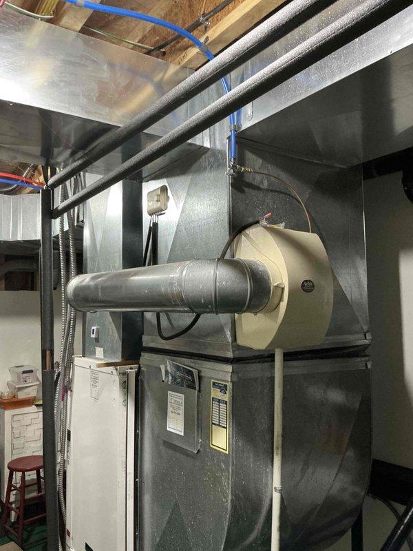 Inspected 20-year-old geothermal HVAC system in basement utility area. Documented existing installation including air handler/furnace unit with metal exhaust vent, ceiling ductwork, and associated connections for potential replacement. Photographs taken of complete system including main unit, ductwork configuration, and electrical components.