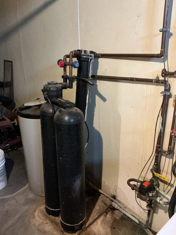 Conducted comprehensive inspection of residential water system to diagnose leaks. Evaluated water softener installation showing two black cylindrical tanks with brine tank, noting deterioration at connection points. Inspected bathtub valve assembly for reported leakage. Documented existing plumbing infrastructure including copper supply lines, galvanized piping, and associated valves for complete assessment and repair recommendation.