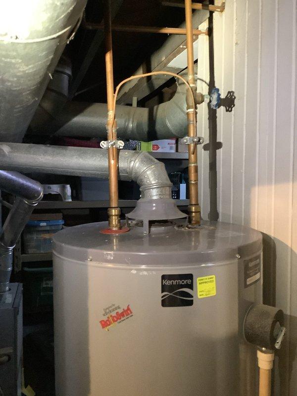 Performed comprehensive inspection of 50-year-old water heater system requiring replacement. Documented existing Kenmore unit with copper pipe connections and metal vent pipe configuration. Evaluated potential Rheem replacement option, noting proper connection requirements for PVC and copper plumbing infrastructure in utility area. Photographs taken of current installation to ensure accurate specifications for replacement proposal.