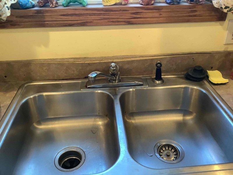 Responded to service call for clogged kitchen sink and leaking faucet. Inspection revealed significant water damage to cabinet flooring beneath sink area, likely from ongoing leak at garbage disposal connection or faucet assembly. Replaced faulty kitchen faucet and cleared drain blockage, restoring proper drainage and eliminating leak.