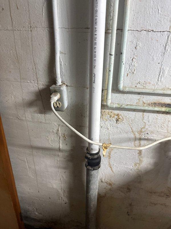 Performed complimentary electrical inspection of unfinished interior space. Examined exposed outlet boxes in main room with tiled flooring that appears to be under renovation. Also inspected electrical outlet and connected power cord in utility area where plumbing pipes are installed, noting wall deterioration including cracks and water stains that could potentially affect electrical safety.