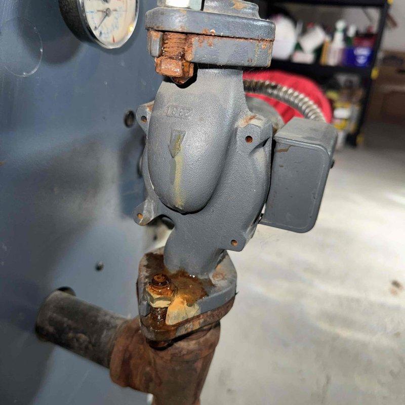 Responded to emergency call for flooded basement caused by boiler pressure safety valve discharge. Upon inspection, found significant corrosion at connection points and valve assembly, particularly at brass fittings showing substantial oxidation. Replaced damaged pressure relief valve to restore proper system operation and prevent further water discharge.