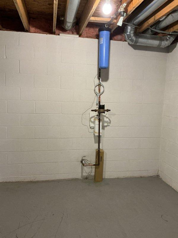 Responded to a service call regarding a water leak identified during a home inspection. Upon examination of the basement plumbing system, which includes a water filtration unit with blue cylindrical tank and associated pipe assembly, no active leaks were detected. Inspected all connections, pressure regulator, and control valves throughout the system, confirming proper operation and integrity of all components.