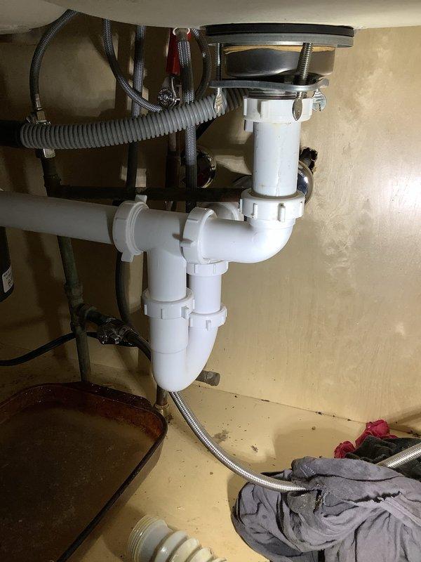 Replaced deteriorated kitchen drain piping in crawlspace, cutting cabinet access point to properly install new PVC trap assembly. Installed approximately 35' of new PVC piping to replace existing horizontal run, connecting to the existing ABS drain line to restore proper drainage function.