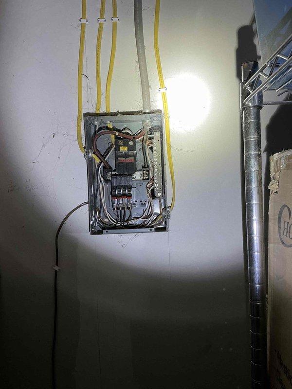 Performed site evaluation for mini split installation in garage space currently operating as an insect breeding business. Inspected electrical panel to assess power availability and identified suitable mounting location on wall with red outline marking. Noted unfinished ceiling with exposed beams and presence of multiple storage containers that will require consideration during system design and installation.