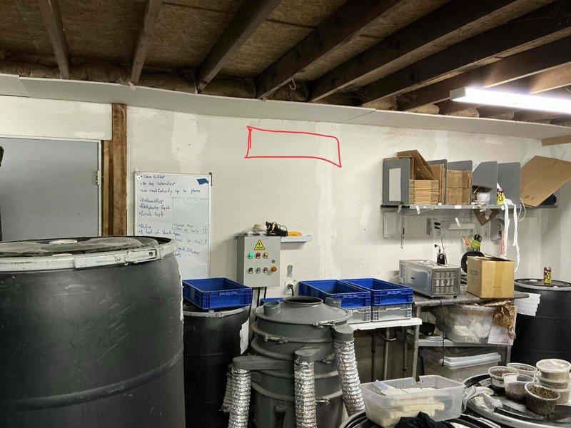 Performed site evaluation for mini split installation in garage space currently operating as an insect breeding business. Inspected electrical panel to assess power availability and identified suitable mounting location on wall with red outline marking. Noted unfinished ceiling with exposed beams and presence of multiple storage containers that will require consideration during system design and installation.