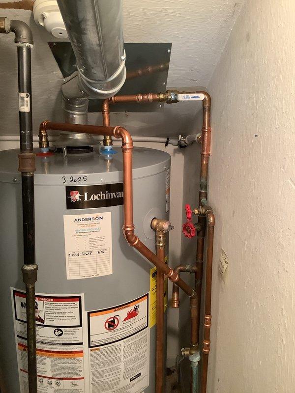 Successfully rerouted water feed line from frozen exterior section to an interior path, running new copper piping above kitchen cabinets, along the kitchen contour, across the living area beam, up to the second floor, and reconnecting to the existing system in the utility room. Abandoned the damaged exterior line in place to prevent further freeze issues. Verified proper operation of the Lochinvar water heater system with all connections secure and leak-free.