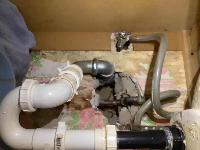 Performed inspection of bathroom sink faucet and surrounding plumbing components for potential replacement. Identified mineral buildup and wear around faucet base, along with makeshift plumbing assembly featuring a combination of PVC pipes, metal fittings, and flexible tubing requiring professional attention.