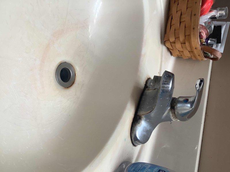 Performed inspection of bathroom sink faucet and surrounding plumbing components for potential replacement. Identified mineral buildup and wear around faucet base, along with makeshift plumbing assembly featuring a combination of PVC pipes, metal fittings, and flexible tubing requiring professional attention.