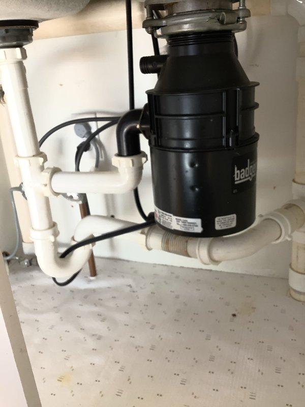 Successfully cleared a double-sided kitchen sink clog that was causing backup in both basins, including the side with the Badger garbage disposal unit. Inspected the under-sink plumbing system, which consists of white PVC pipes forming a P-trap configuration, and verified proper drainage after service was completed.