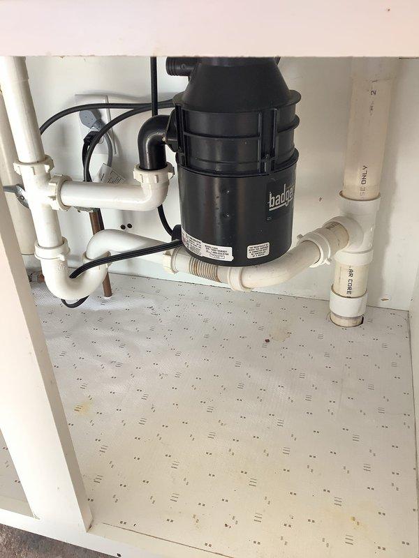 Successfully cleared a double-sided kitchen sink clog that was causing backup in both basins, including the side with the Badger garbage disposal unit. Inspected the under-sink plumbing system, which consists of white PVC pipes forming a P-trap configuration, and verified proper drainage after service was completed.