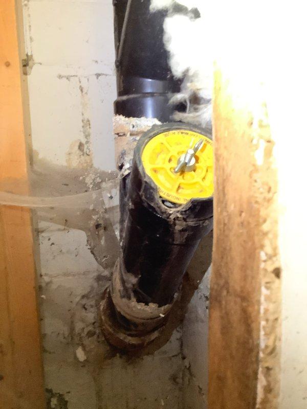 Completed inspection and repair work on main sewer line Y fitting in 100-year-old owner-occupied duplex. Accessed exposed plumbing through interior wall section where black PVC pipe and yellow valve assembly were visible. Also addressed damaged water line connected to exterior hose bibb, which required accessing the large black ventilation ductwork in the utility area where the damaged line was located among wooden framing elements and insulation.