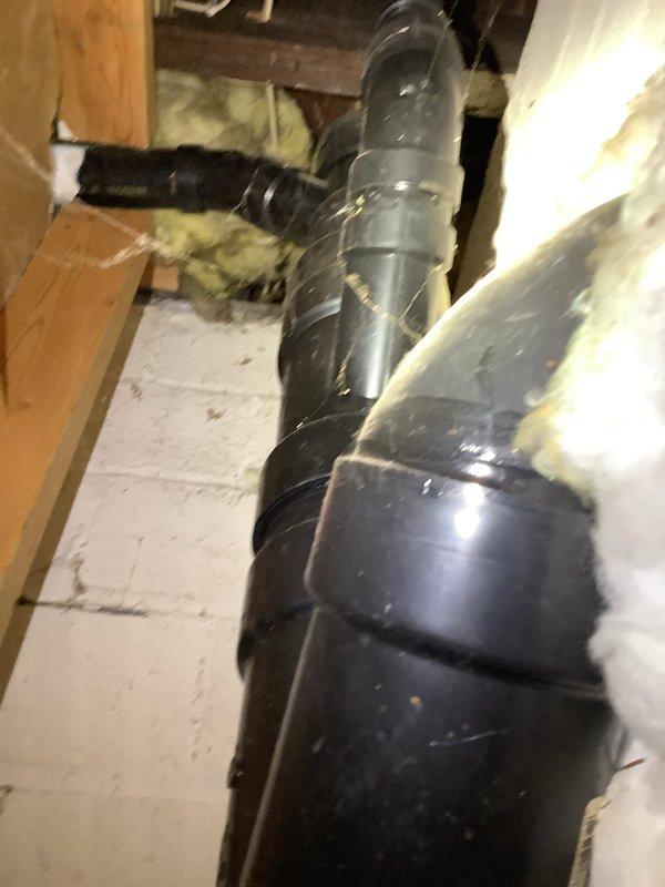 Completed inspection and repair work on main sewer line Y fitting in 100-year-old owner-occupied duplex. Accessed exposed plumbing through interior wall section where black PVC pipe and yellow valve assembly were visible. Also addressed damaged water line connected to exterior hose bibb, which required accessing the large black ventilation ductwork in the utility area where the damaged line was located among wooden framing elements and insulation.