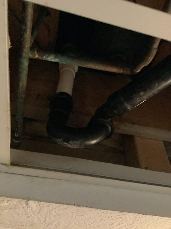 Responded to service call for clogged bathtub drain. Inspection revealed significant mineral deposits and rust staining around bathroom sink drain and basin. Performed drain clearing service on the affected plumbing system, which included accessing and clearing the black ABS drain pipe with elbow joint connected to PVC piping beneath the structure.