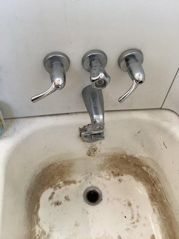 Responded to service call for clogged bathtub drain. Inspection revealed significant mineral deposits and rust staining around bathroom sink drain and basin. Performed drain clearing service on the affected plumbing system, which included accessing and clearing the black ABS drain pipe with elbow joint connected to PVC piping beneath the structure.