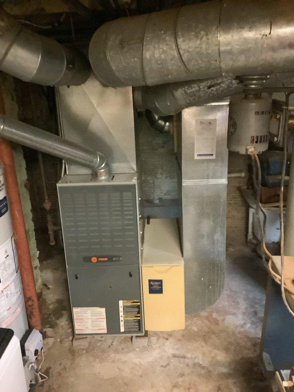 Completed installation of a new complete HVAC system, including a Trane furnace with connected ductwork in the basement utility area and a Lennox outdoor AC condenser unit (80 AC 600 model). System was properly mounted with all necessary connections, including refrigerant lines running to the house, and the outdoor unit was positioned on a mounting pad adjacent to the home's exterior.