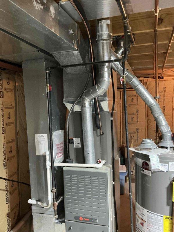 Performed comprehensive inspection of 21-year-old Trane furnace system in residential basement mechanical room. Evaluated existing ductwork connections, supply plenum, and exhaust venting. Provided replacement estimate for aging unit, documenting current installation configuration alongside adjacent water heater to ensure proper system compatibility for potential upgrade.