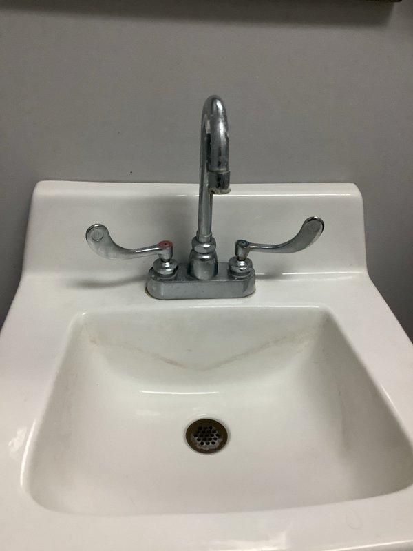 Provided comprehensive estimate for commercial fixture installation including two new toilets, two new sinks, and replacement of two faucets on existing sink. Proposal also includes installation of new hot water tank with associated hot/cold water supply lines. Documented current plumbing conditions with photos showing existing wall-mounted porcelain sink with chrome fixtures exhibiting normal wear and standard under-sink plumbing components in functional condition.