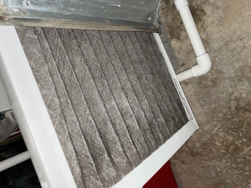 Performed scheduled maintenance service on 2-year-old central air conditioning system. Inspected furnace installation in basement, noting proper mounting on wooden platform with connected PVC condensate drain system and copper refrigerant lines. Examined air filter, which showed significant dust accumulation requiring replacement to maintain system efficiency and proper airflow.