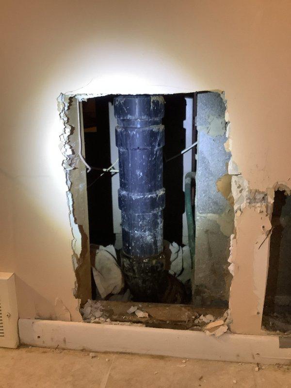 Repaired a leaking main drain stack located just above the concrete entry point by accessing the pipe through a rectangular cutout in the drywall. Documented existing damage to the lower section of the wall where the stack is located, including the exposed pipe connections requiring service.