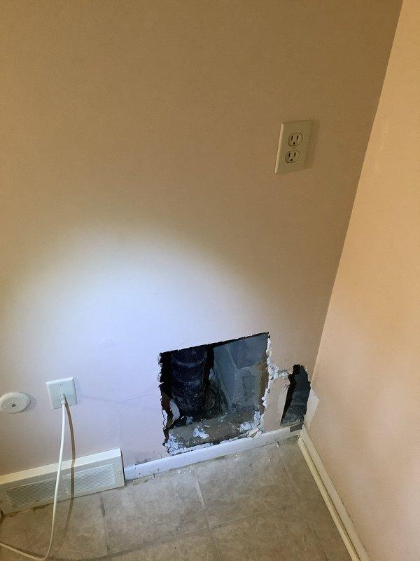 Repaired a leaking main drain stack located just above the concrete entry point by accessing the pipe through a rectangular cutout in the drywall. Documented existing damage to the lower section of the wall where the stack is located, including the exposed pipe connections requiring service.