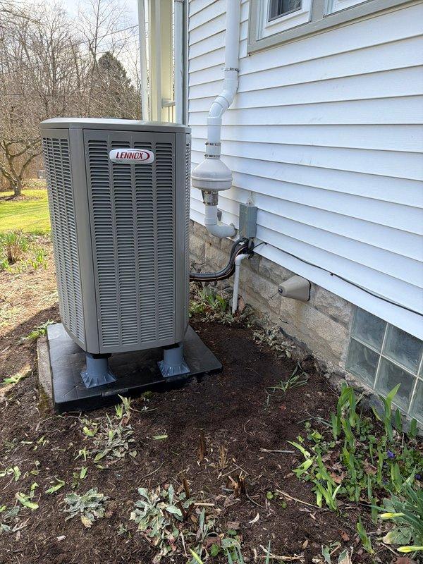 Completed installation of new Lennox dual-fuel HVAC system consisting of an oil furnace and heat pump. System includes proper condensate drainage with PVC piping and trap assembly. Unit was mounted on a stable black pad with appropriate clearances, and all refrigerant lines and electrical connections were professionally secured to the exterior of the home.