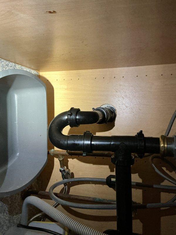 Responded to a customer service call regarding a backed-up kitchen sink in a 20-year-old residence. Upon inspection, found clogged drainage system requiring cleaning of P-trap and associated piping. Successfully cleared blockage and verified proper drainage function by testing water flow through the newly serviced system. Documented completed work with photos showing the under-sink plumbing configuration and connected drainage components.