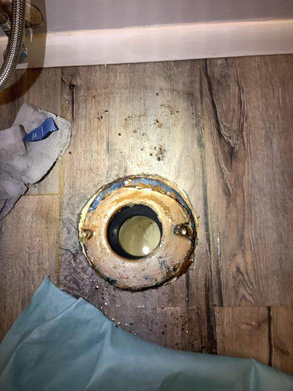Responded to service call for toilet leaking at base. Upon inspection, discovered significant water damage to flooring and a severely corroded toilet flange. Removed toilet, assessed damage, replaced flange and wax ring, then reinstalled and sealed toilet. Verified proper operation with no leaks after repair.