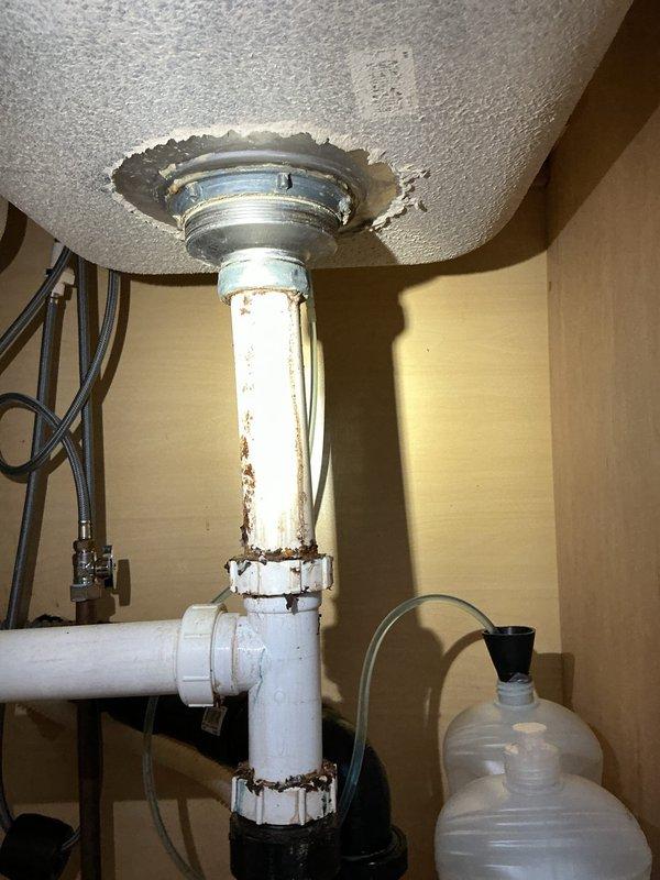 Responded to kitchen sink leak call. Discovered significant corrosion and deterioration at drain pipe connections under sink, particularly at the metal fitting where the PVC pipe enters the sink basin. Replaced damaged components and secured all connections to eliminate leak.