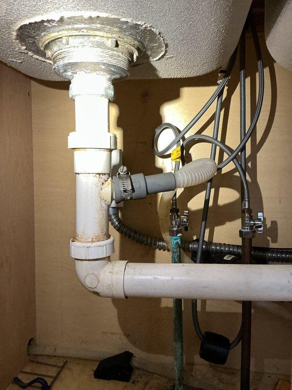Responded to kitchen sink leak call. Discovered significant corrosion and deterioration at drain pipe connections under sink, particularly at the metal fitting where the PVC pipe enters the sink basin. Replaced damaged components and secured all connections to eliminate leak.