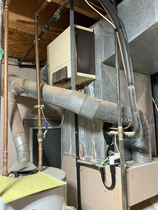 Performed inspection for potential replacement of 35-year-old furnace and central AC system in residential property. Current installation features an aging HVAC unit with extensive galvanized metal ductwork and copper refrigerant lines showing signs of normal wear. Documented existing system configuration in basement/utility room, including connections to water heater and electrical components, to prepare comprehensive replacement estimate.