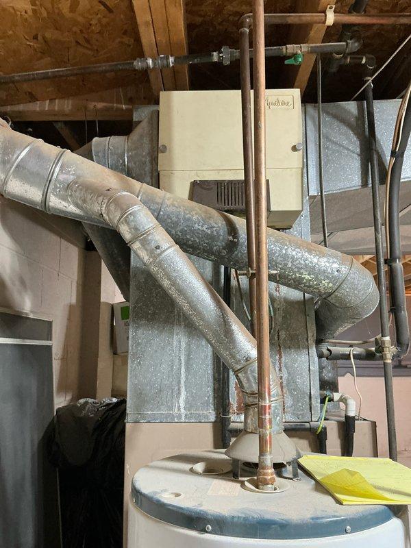 Performed inspection for potential replacement of 35-year-old furnace and central AC system in residential property. Current installation features an aging HVAC unit with extensive galvanized metal ductwork and copper refrigerant lines showing signs of normal wear. Documented existing system configuration in basement/utility room, including connections to water heater and electrical components, to prepare comprehensive replacement estimate.