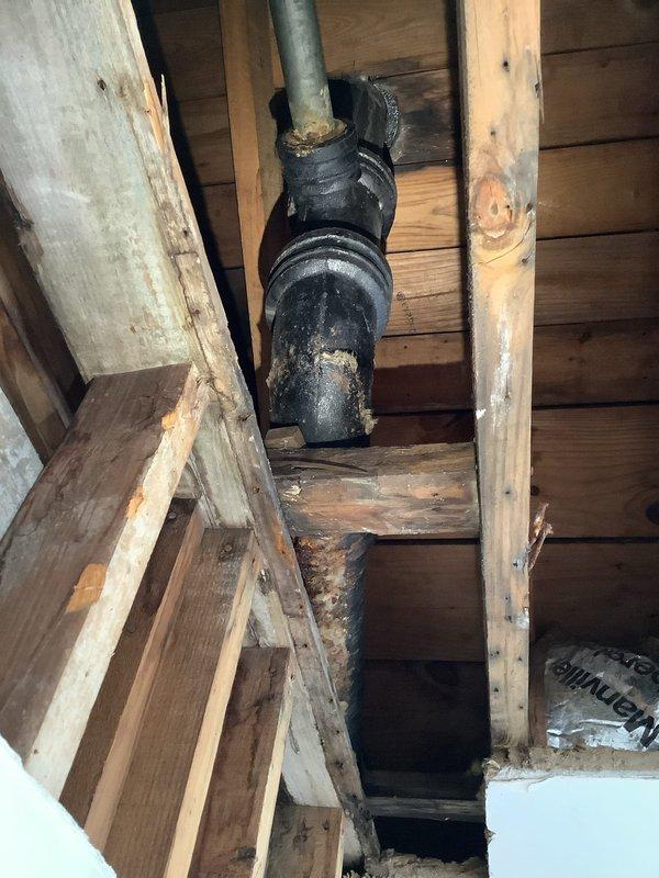 Inspected deteriorating stack pipe identified by previous water damage assessment team. Observed black PVC waste pipe with multiple connection points running vertically through wooden joists showing signs of moisture damage. Documented condition of T-junction and connecting fittings where leakage was evident. Prepared detailed quote for replacement of compromised section of drainage system to prevent further structural damage to surrounding wooden framework.