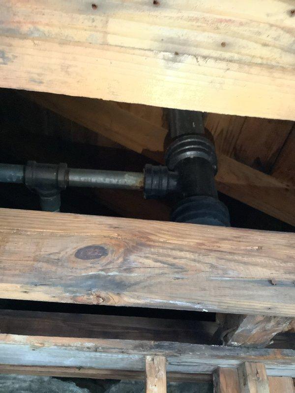Inspected deteriorating stack pipe identified by previous water damage assessment team. Observed black PVC waste pipe with multiple connection points running vertically through wooden joists showing signs of moisture damage. Documented condition of T-junction and connecting fittings where leakage was evident. Prepared detailed quote for replacement of compromised section of drainage system to prevent further structural damage to surrounding wooden framework.