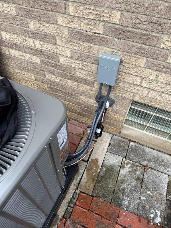 Installed new 90K BTU Lennox air conditioning system with outdoor condenser unit properly mounted on code-compliant pad adjacent to home exterior. Completed electrical connections via wall-mounted disconnect box with appropriate conduit and power lines. System was tested and verified to be functioning according to manufacturer specifications.