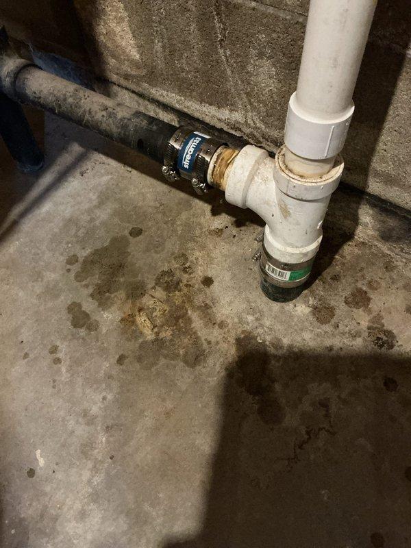 Repaired split ABS kitchen drain line by cutting pipe below floor level and installing approved transition coupling to connect ABS to PVC. Rebuilt drainage system and tied back to vertical PVC pipe with standard coupling. Replaced lower fernco with approved transition coupling on horizontal pipe to laundry tub, resolving leak issues.