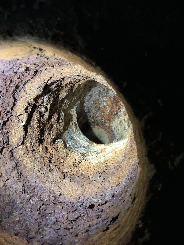Responded to service call for sewer line backup in basement with associated odor. Inspection revealed deteriorated sewer drain pipe with significant mineral buildup and structural cracks causing blockage. Successfully cleared obstruction and documented condition of aging infrastructure with recommendation for future pipe replacement due to visible deterioration of interior surfaces.