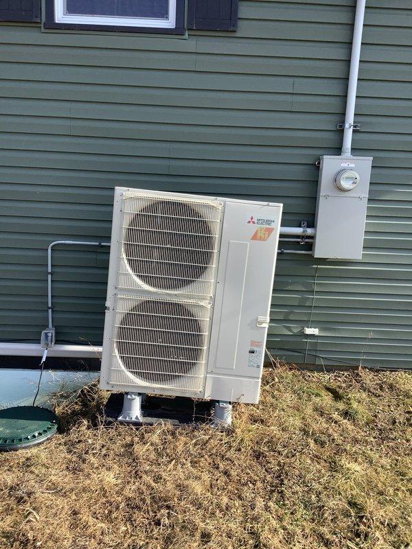 Identified burrowing animal damage under Mitsubishi heat pump outdoor unit causing instability. Documented condition with photos showing unit on uneven concrete pad with exposed soil underneath. Leveled unit with stone to prevent further animal intrusion and ensure proper equipment operation.