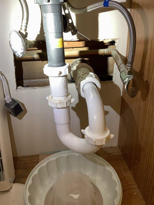 Repaired leaking drain assembly under bathroom vanity by replacing deteriorated green pipe section with new PVC P-trap configuration. Installed water catch container as precautionary measure and verified proper drainage with no leaks after completion.